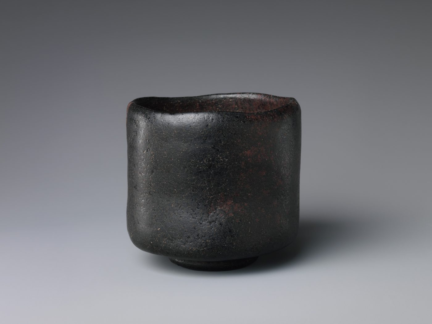 A black, hand-formed earthenware tea bowl with straight, slightly uneven sides and a matte, faintly mottled surface.